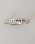 A silver stacking ring with the name 'sawyer' engraved on it, displayed against a white background.