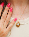 Gold necklace with a pendant worn by a person with pink nail polish.