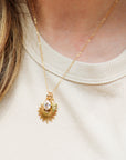 Gold necklace with a pendant worn by a person on a beige background