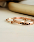 A photo showing a gold-colored ring with the name 'Charlie' engraved on it, worn on a person's finger.