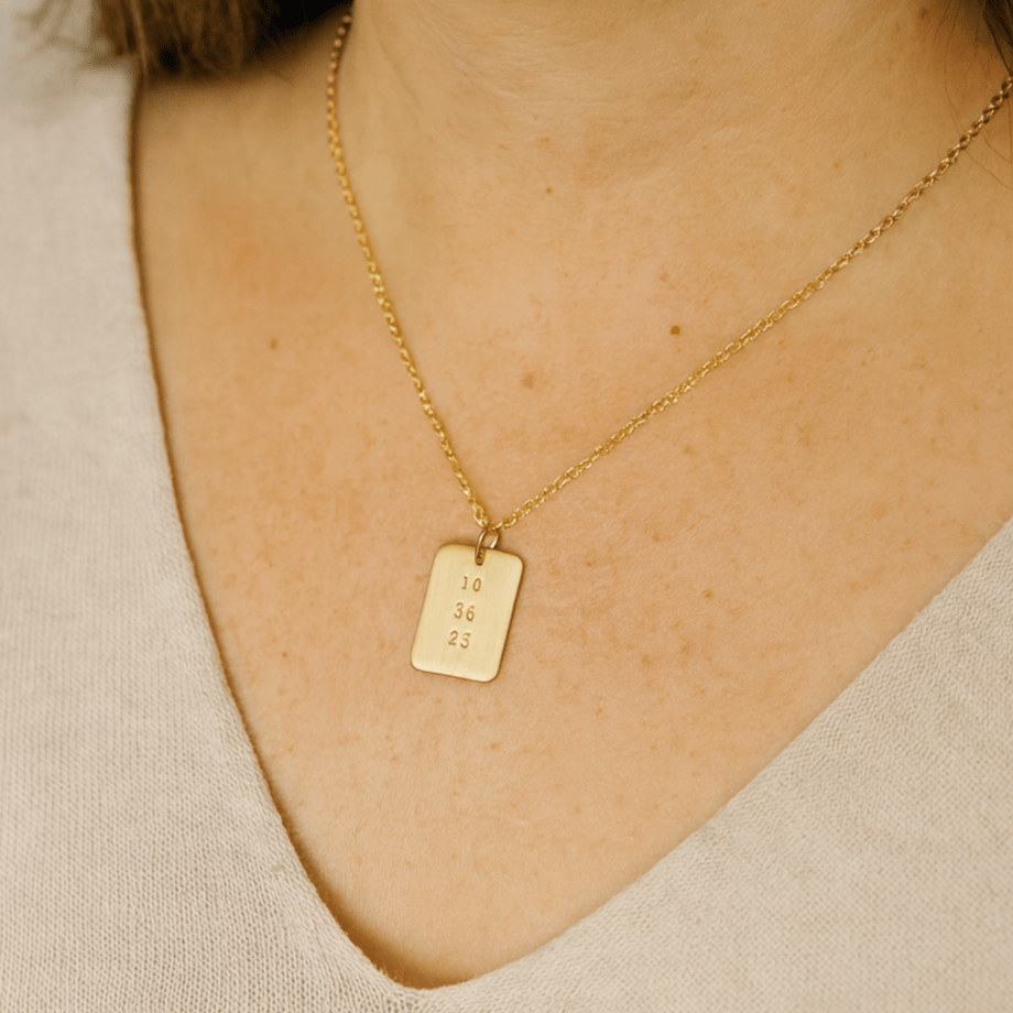 Woman wearing gold date-stamped pendant necklace with gold chain against a neutral top
