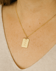 Woman wearing gold date-stamped pendant necklace with gold chain against a neutral top