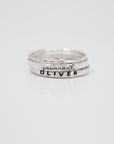 A set of three rings, including two name rings in different fonts and a clear birthstone ring, displayed against a white background.