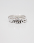 A set of three rings, including two name rings in different fonts and a clear birthstone ring, displayed against a white background.