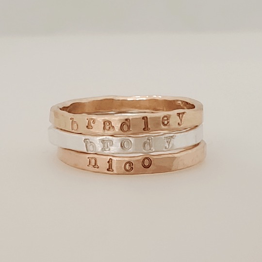 Stacked hand stamped name rings in silver and gold with personalized inscriptions bradley, brody, and nico
