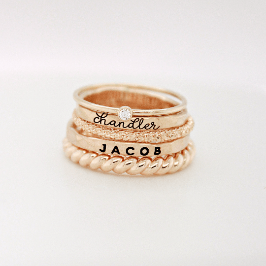 Custom name ring set for women with mixed metal stacking rings in gold and silver featuring personalized names and a small gemstone detail.