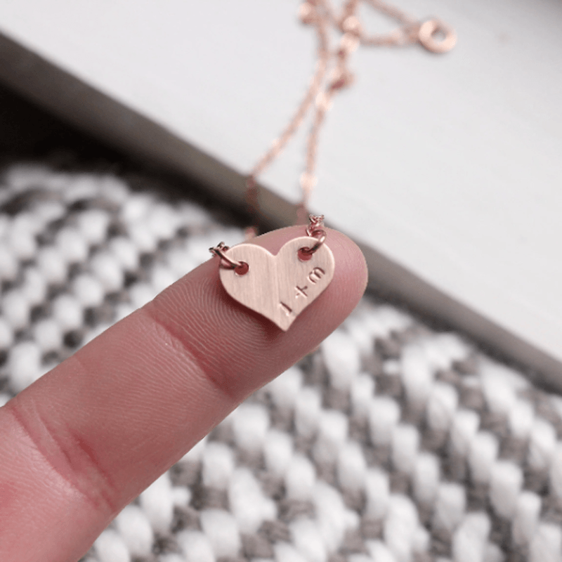 Close-up of hand stamped initial heart necklace pendant on finger with rose gold chain