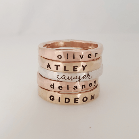 Thick personalized stacking rings in silver, yellow gold, and rose gold with engraved names and hammered finish