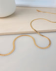 A gold herringbone necklace with a lobster clasp, laid out on a flat surface.