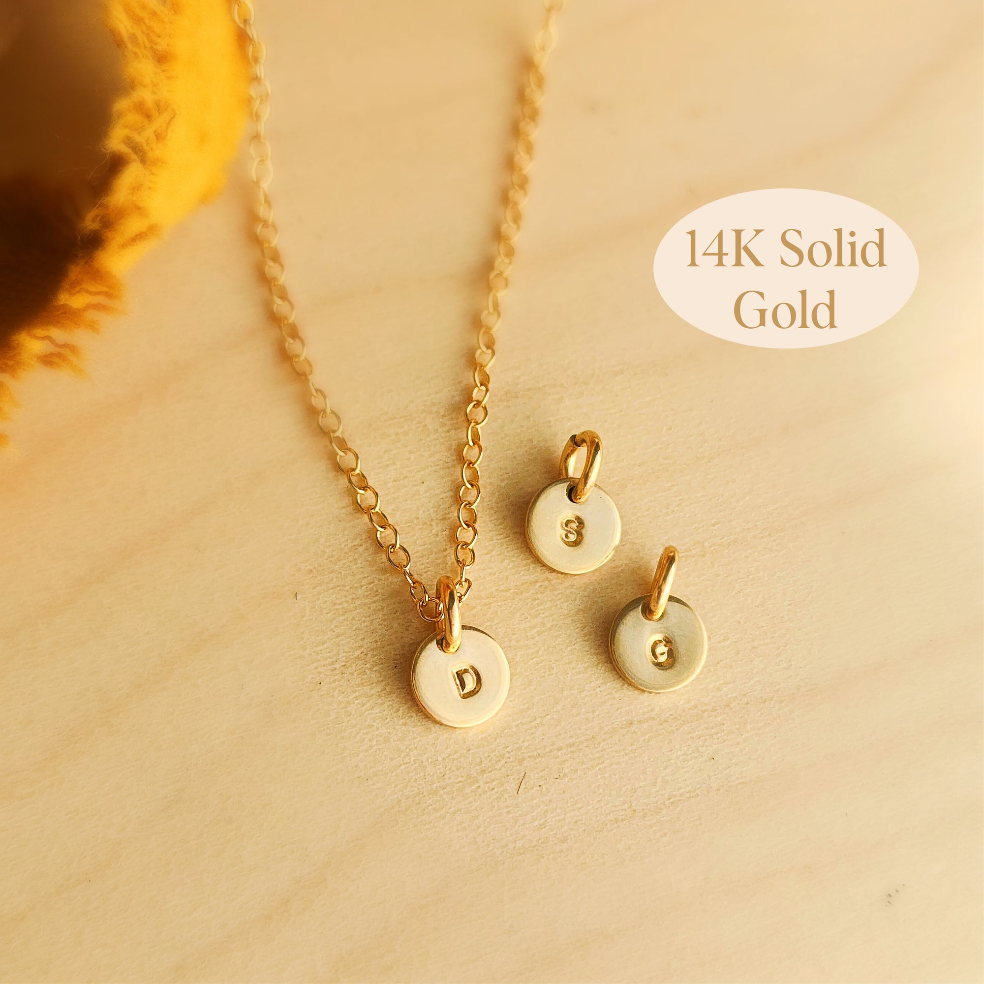 Three 14K solid gold dainty initial necklaces with round engraved tags on wood background