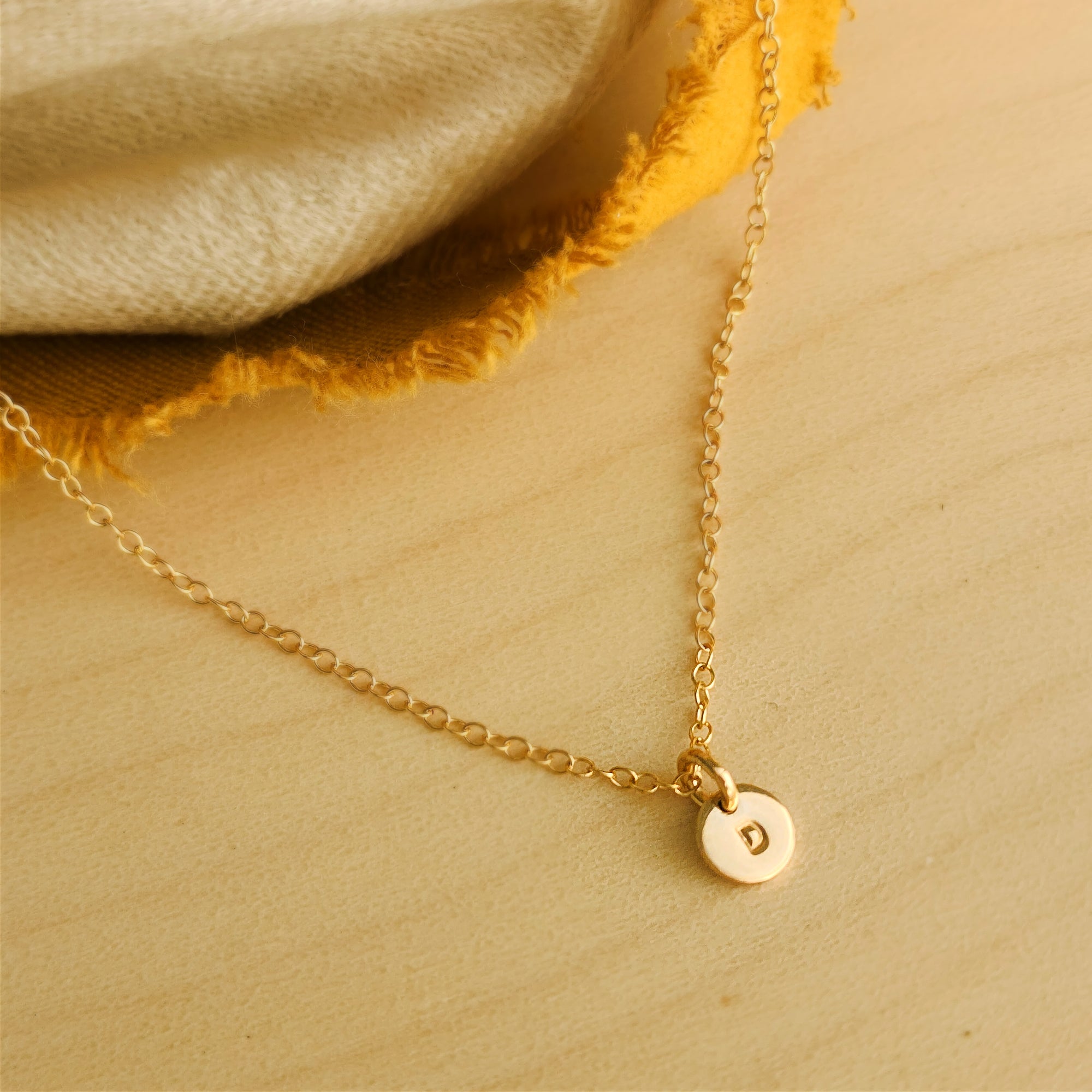 Flat lay of 14K solid gold dainty initial necklace on soft beige fabric