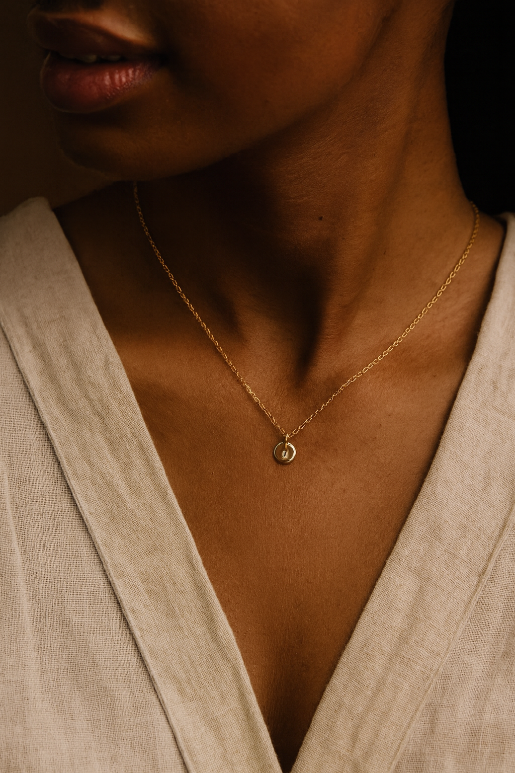 14K solid gold dainty initial necklace worn by woman with dark skin and linen blouse, handcrafted jewelry close-up