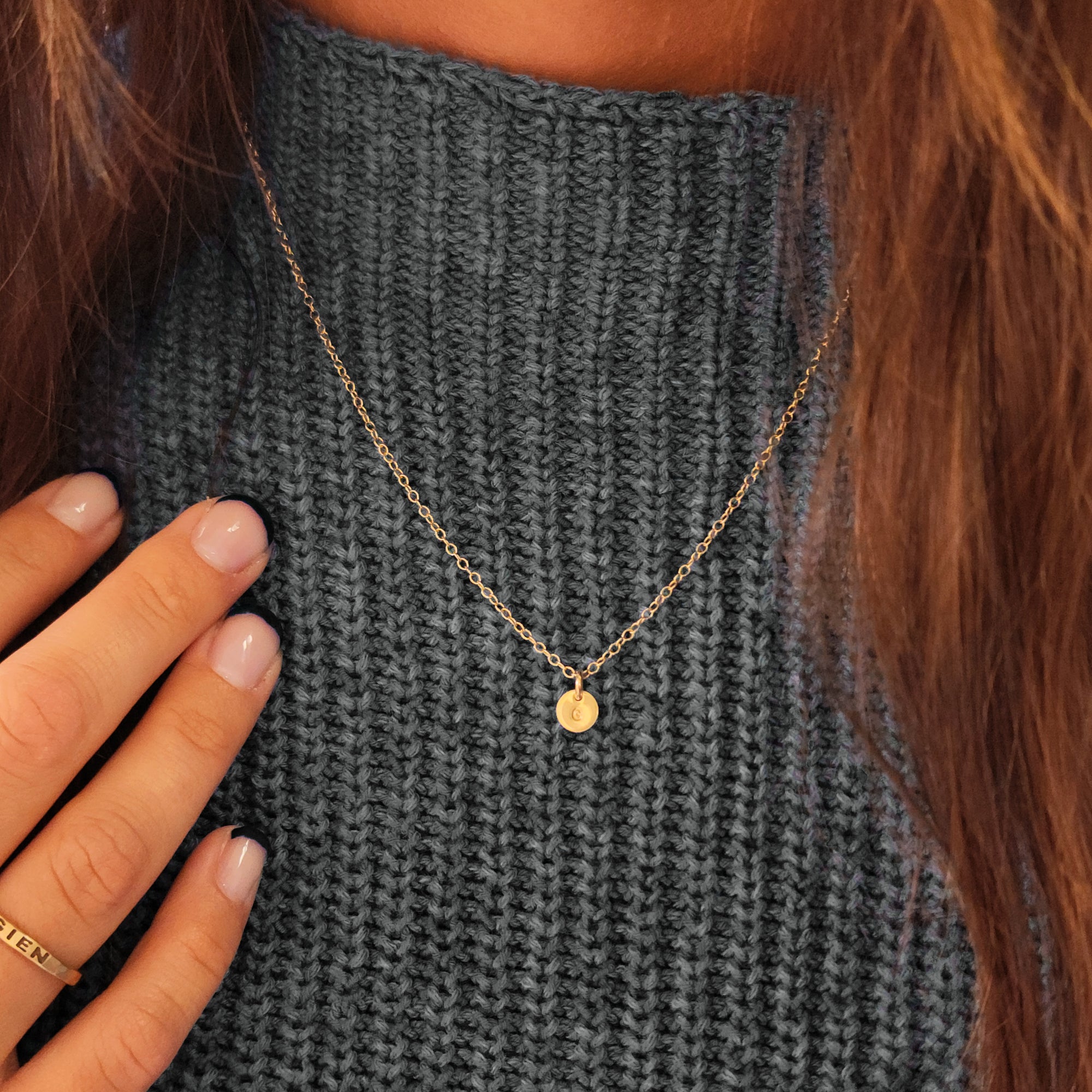 Woman wearing 14K solid gold dainty initial necklace over a gray sweater