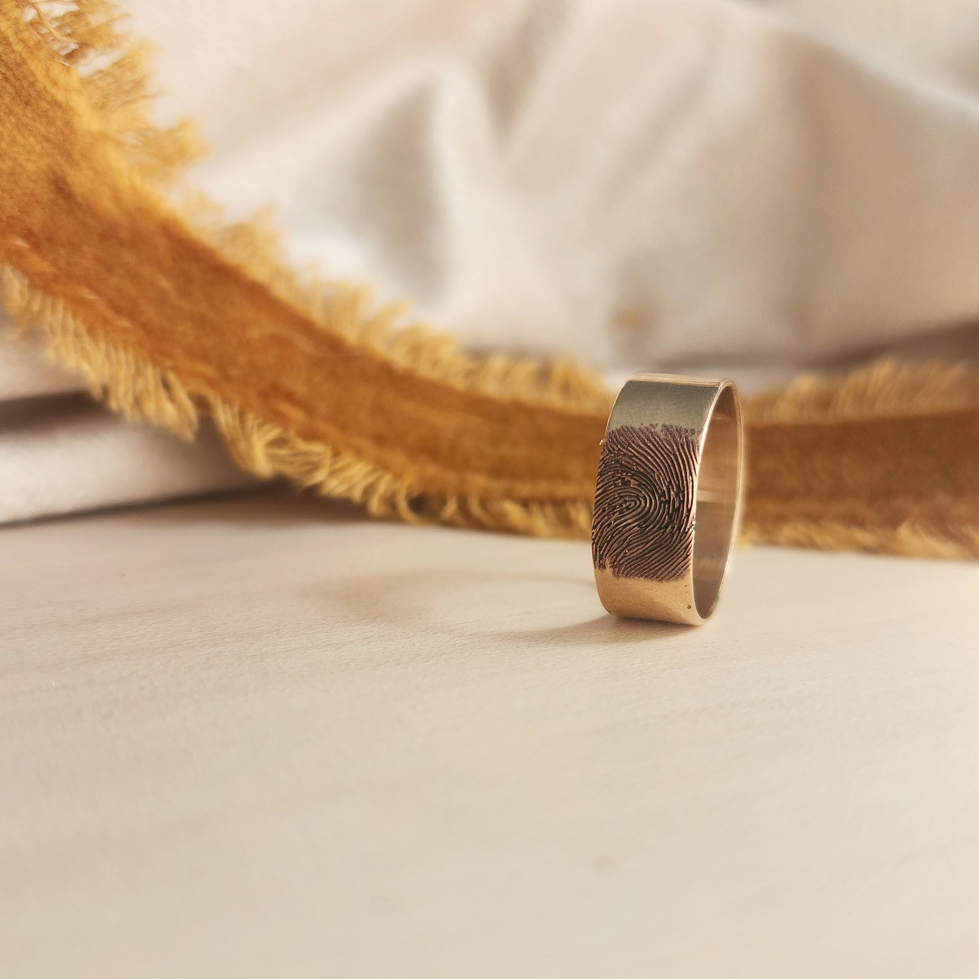 14K solid gold fingerprint band on wood surface with dramatic shadowing