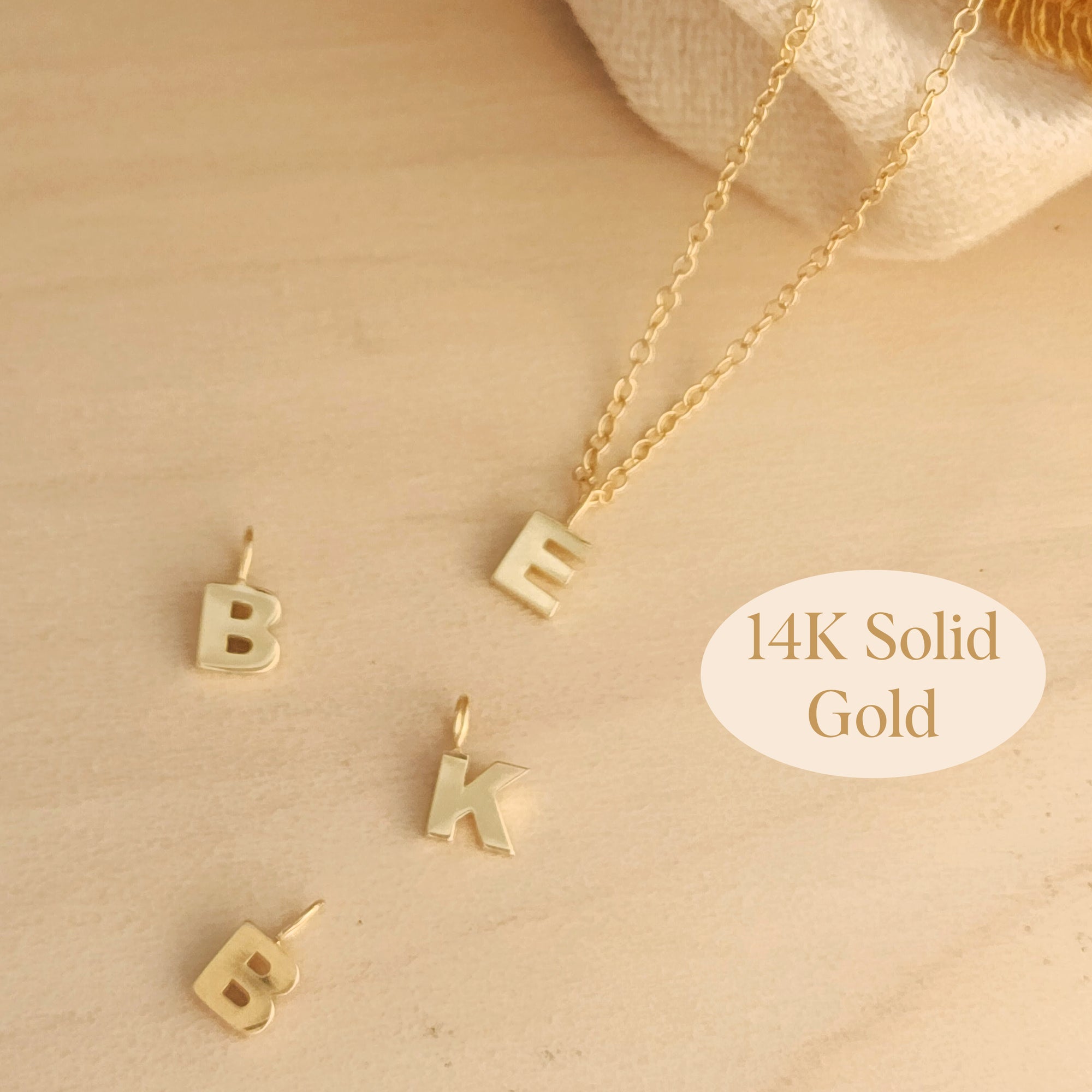 Flat lay of 14K solid gold initial pendant necklace with B, K, and E charms on wood background