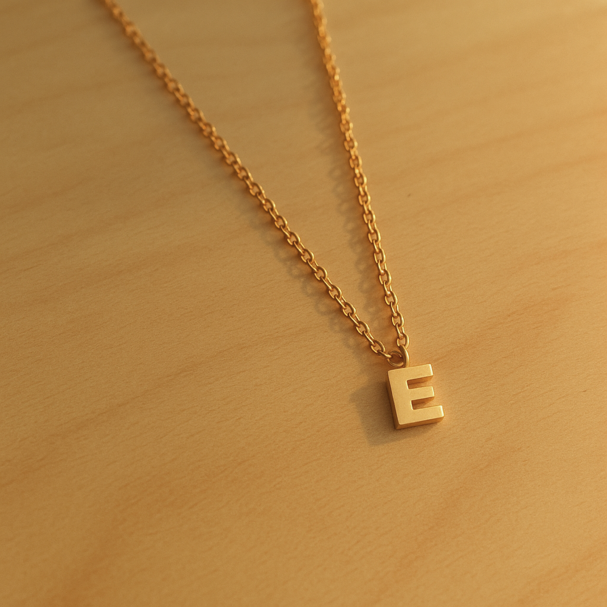 Close-up of 14K solid gold initial pendant necklace with E charm on wood surface
