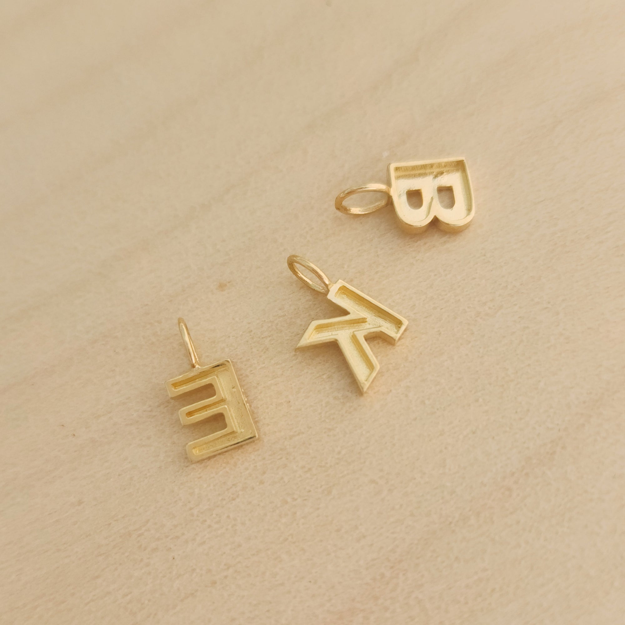 Loose 14K solid gold initial charms B, K, E arranged on wood background