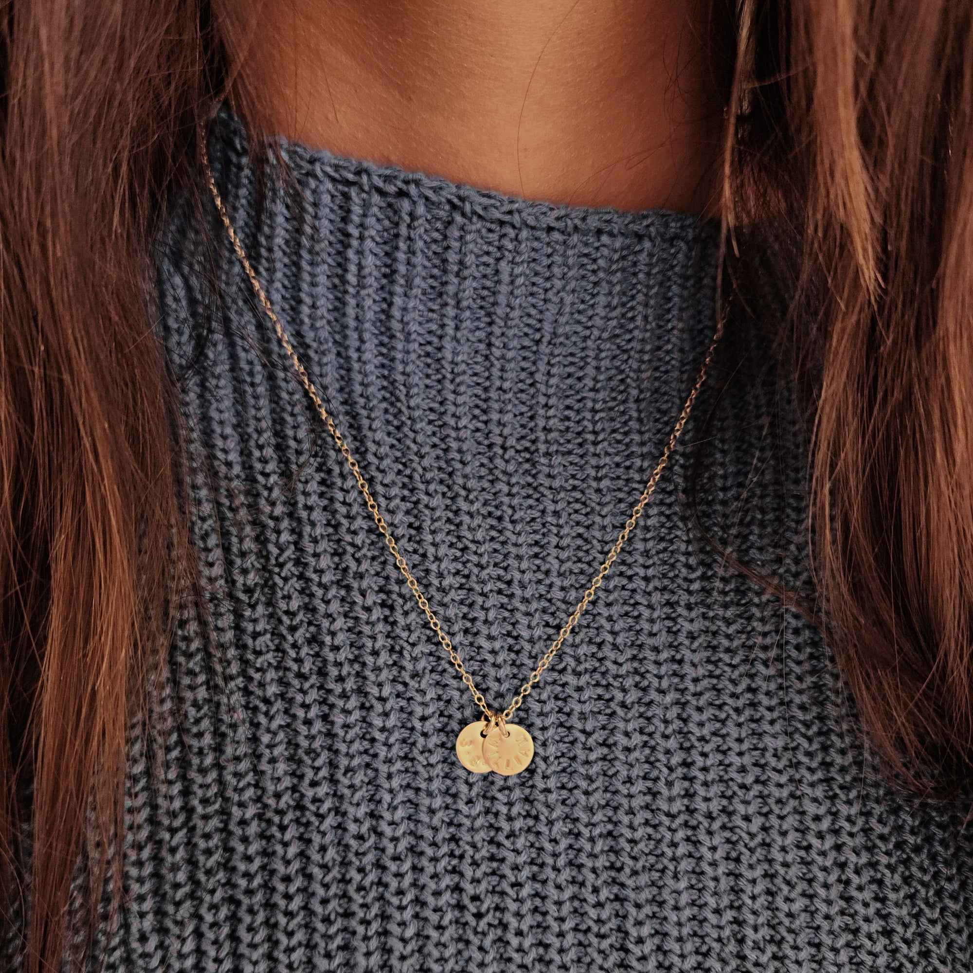 Close-up of two round tags on 14K solid gold name necklace over light wood