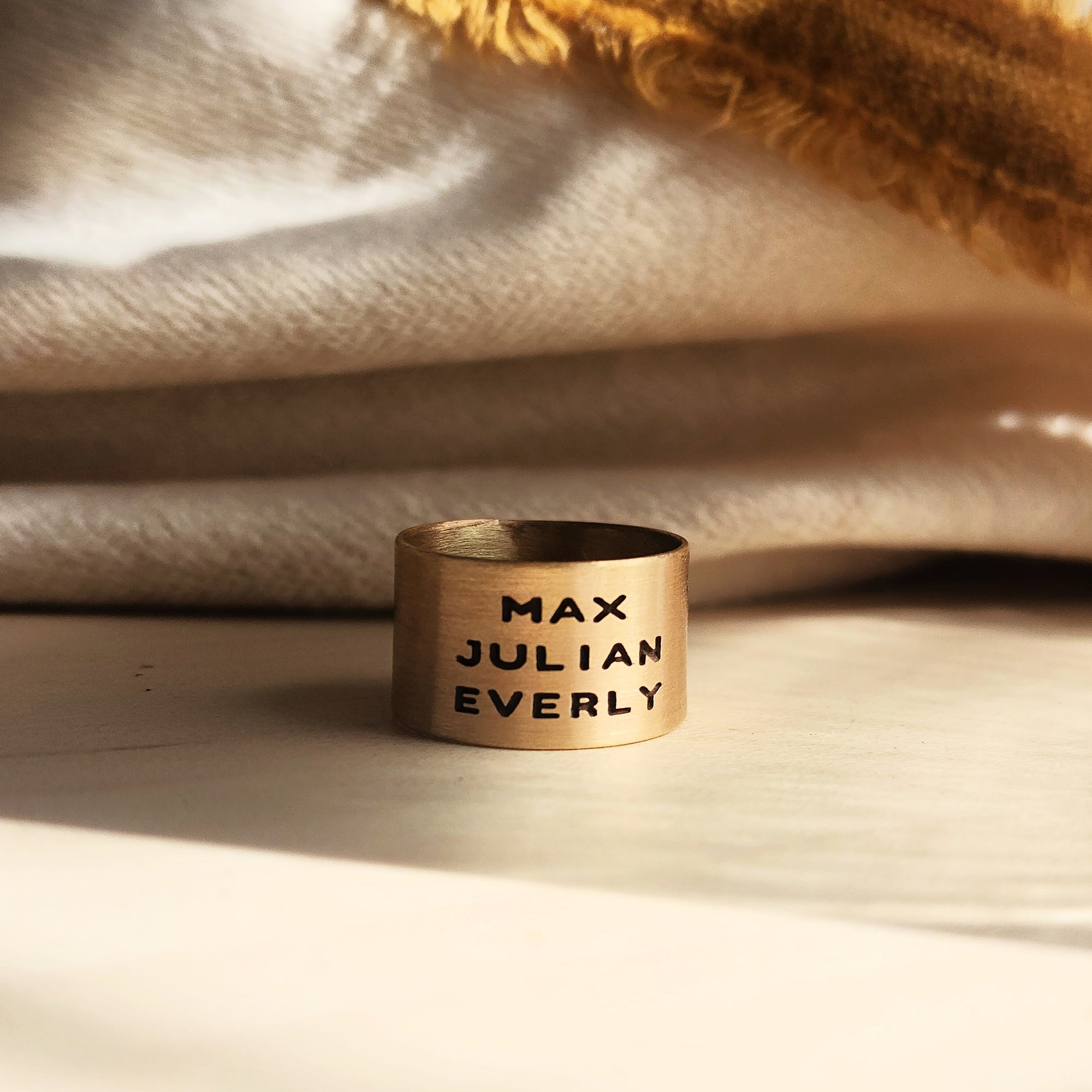 14K solid gold personalized band engraved with names resting on cozy textured fabric