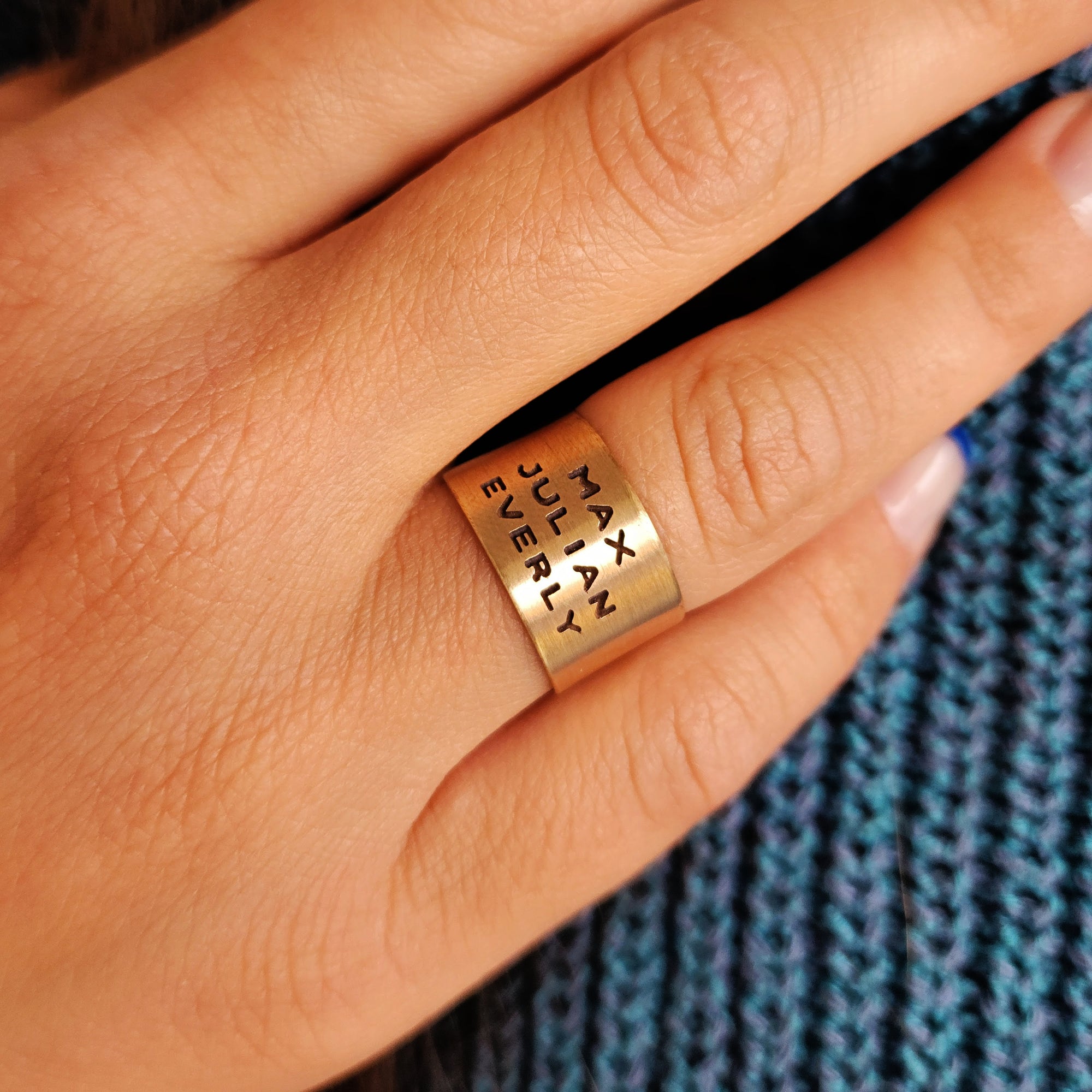 Close-up of 14K solid gold personalized band worn on model’s finger with visible engravings