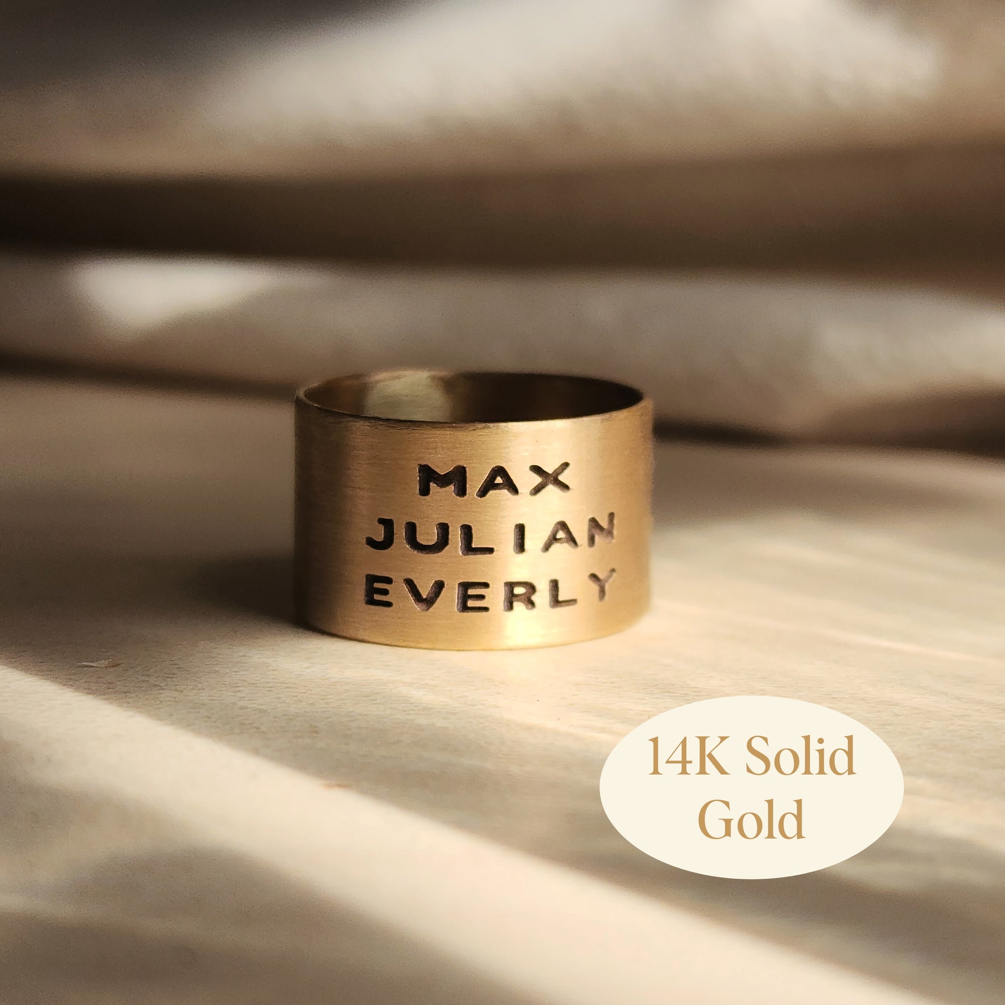14K solid gold personalized band engraved with names Max, Julian, and Everly on soft background