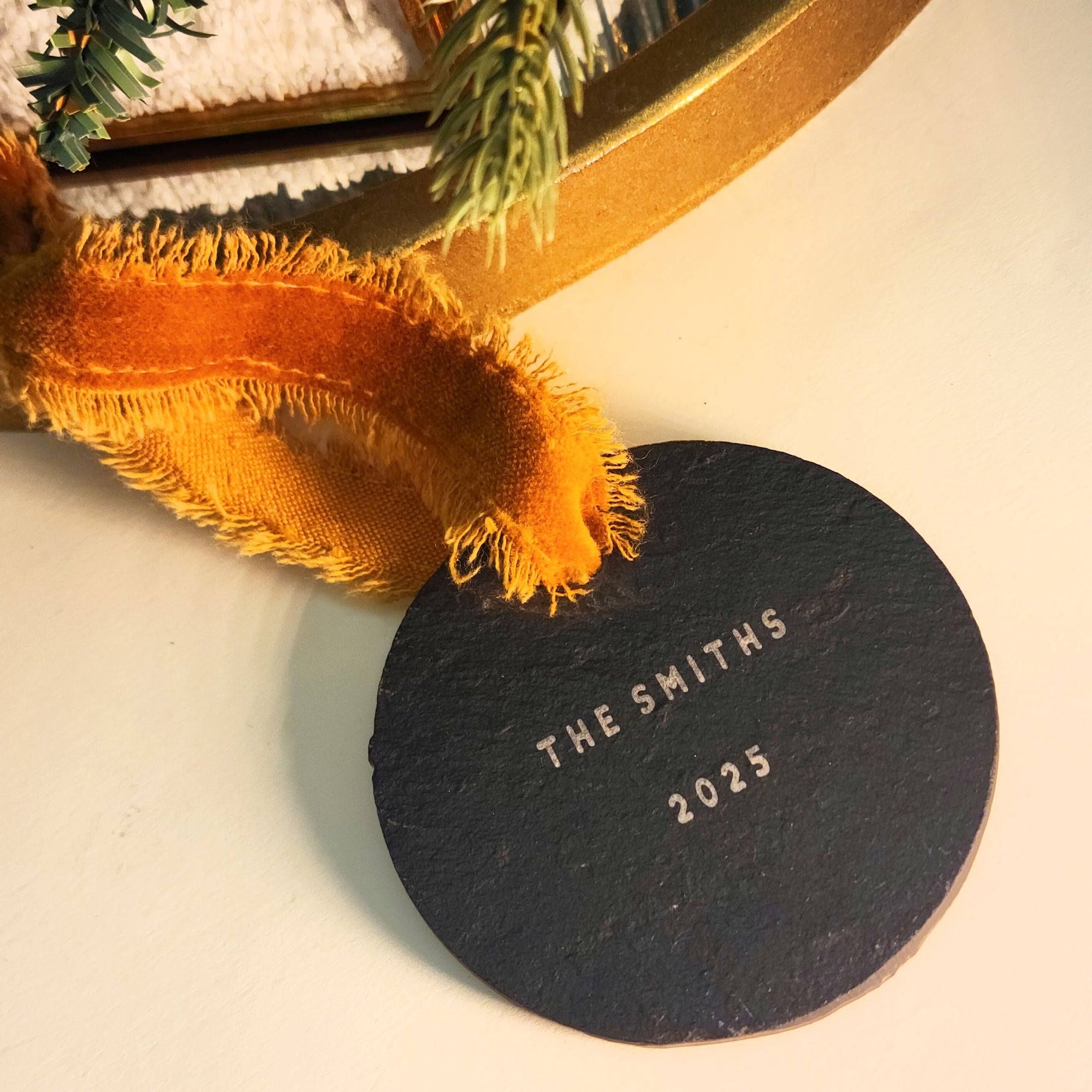 Round black tag with 'The Smiths 2025' text on a decorative background with orange fabric and greenery.
