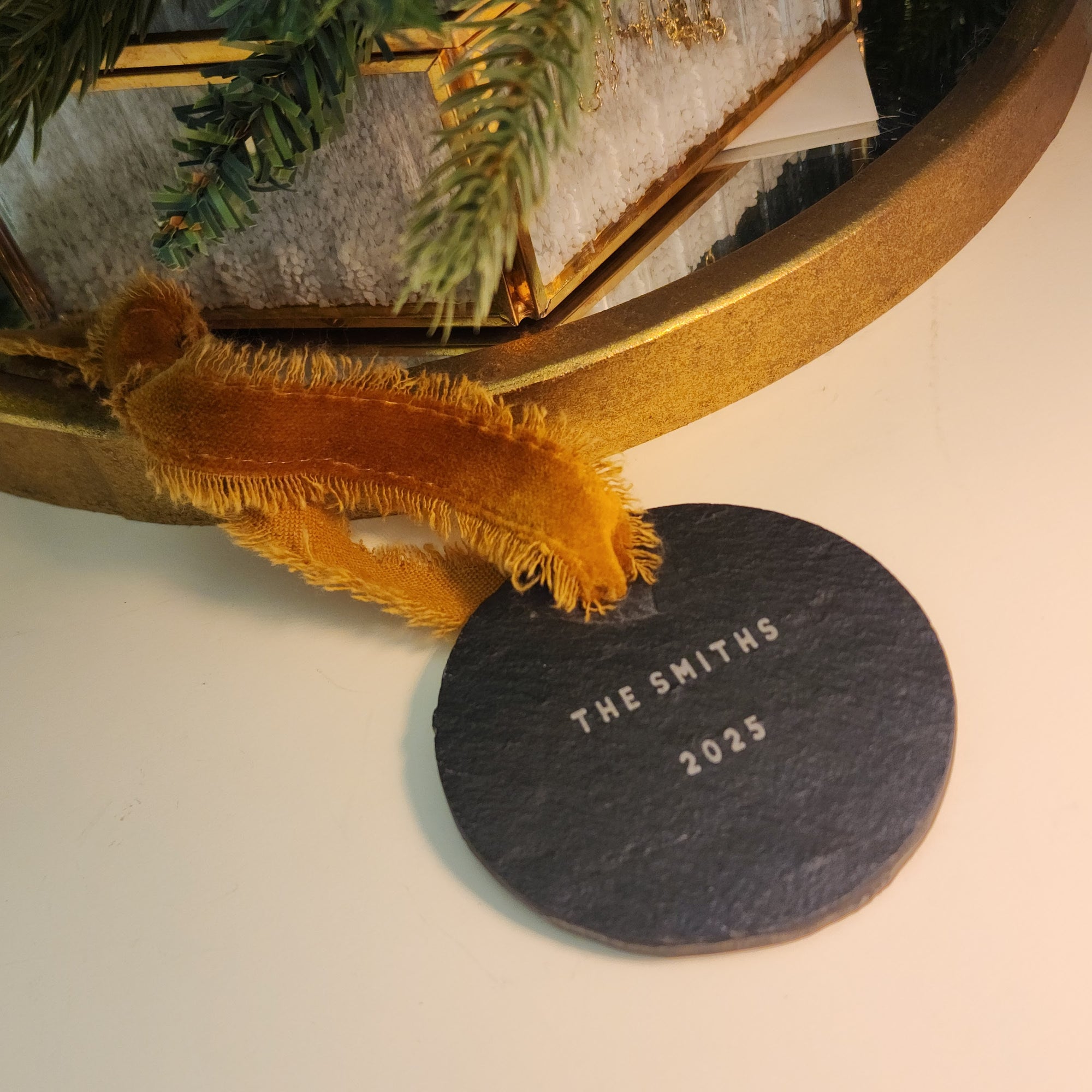 Decorative slate disc with 'The Smiths 2025' text, placed on a surface with a gold frame and greenery.