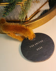 Decorative slate disc with 'The Smiths 2025' text, placed on a surface with a gold frame and greenery.