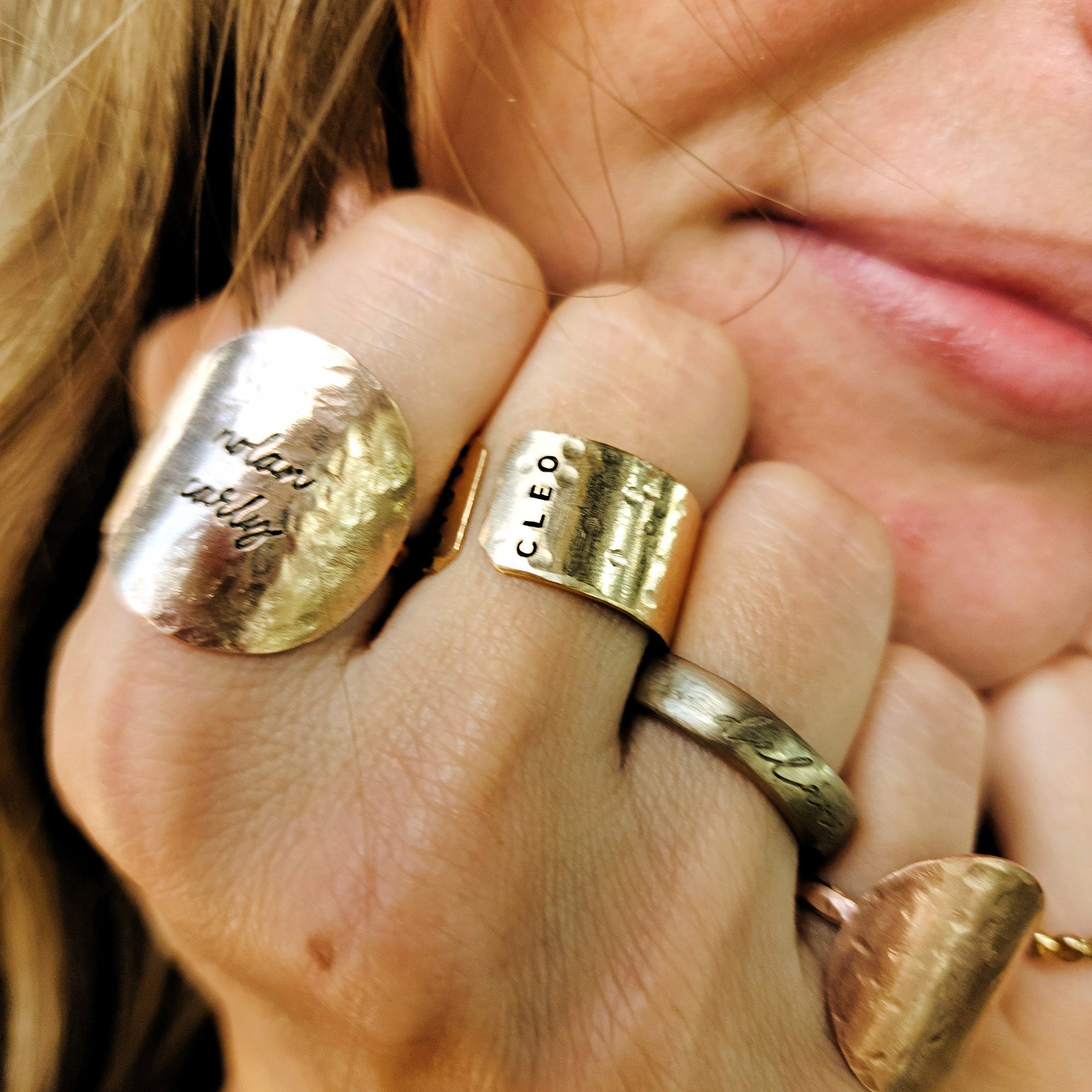 Close-up of a hand wearing multiple gold rings with visible branding.
