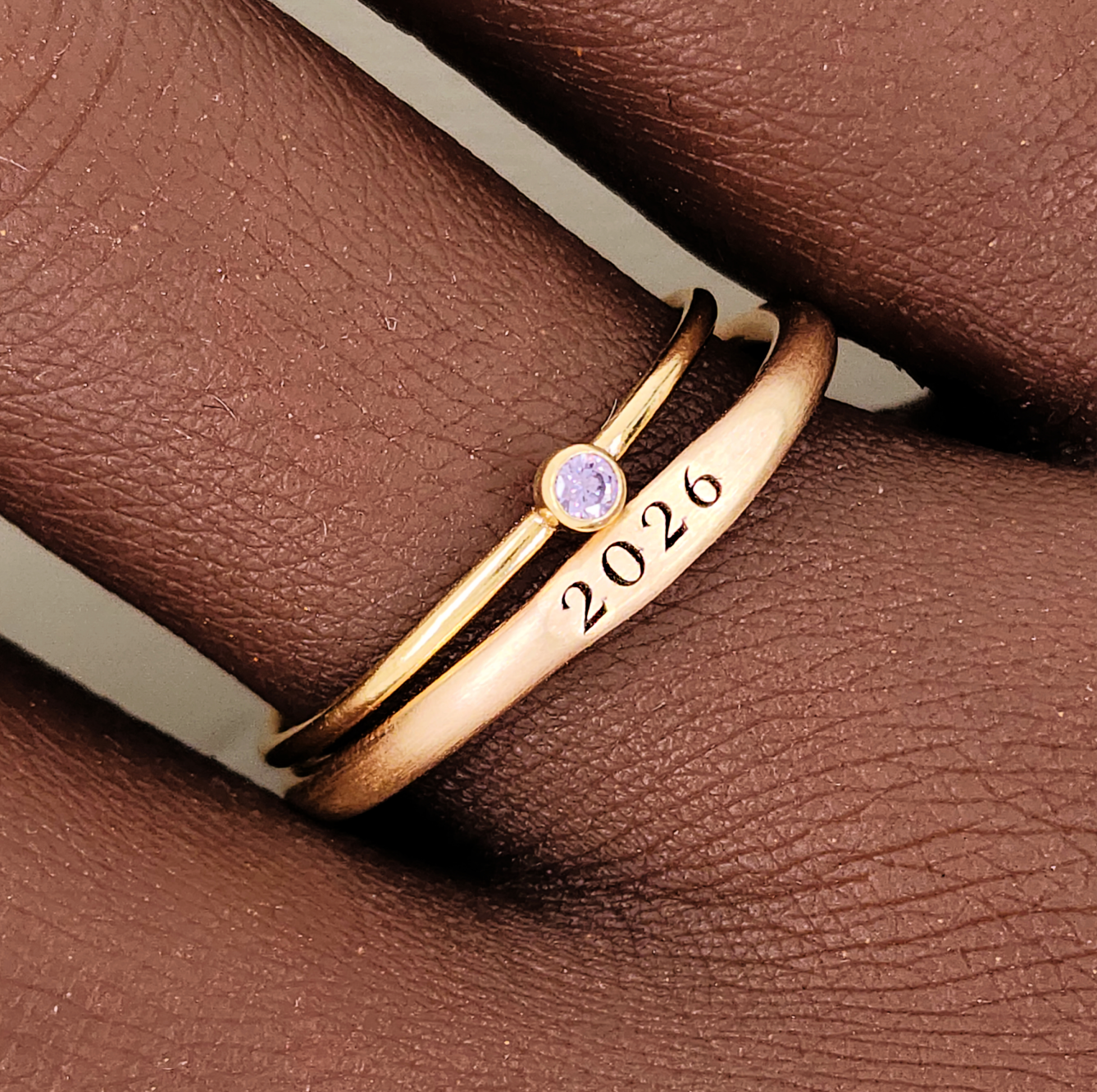 Two rings, one with a plain band and the other featuring a birthstone, displayed on a textured surface with a soft shadow.