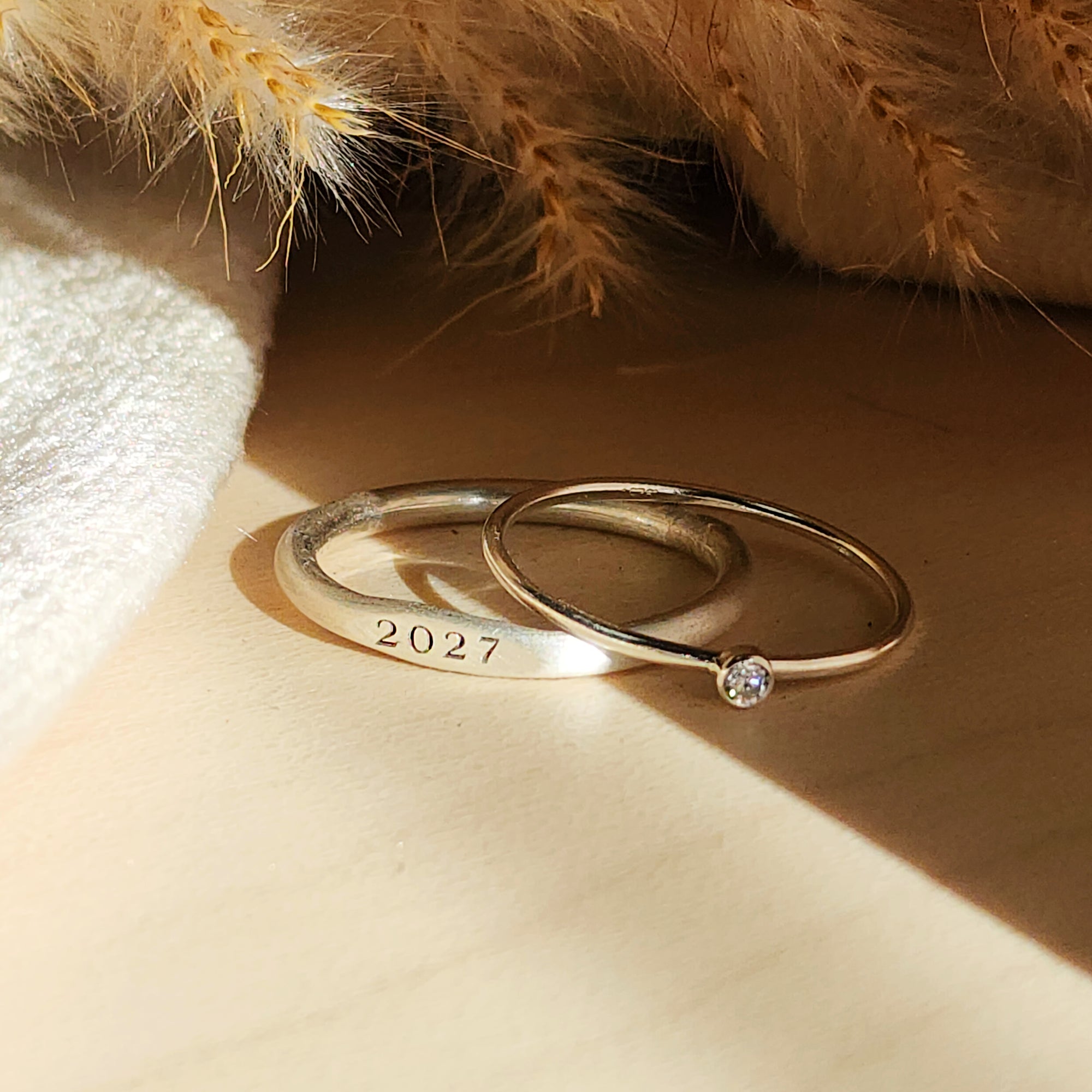 Two rings, one with a plain band and the other featuring a birthstone, displayed on a textured surface with a soft shadow.