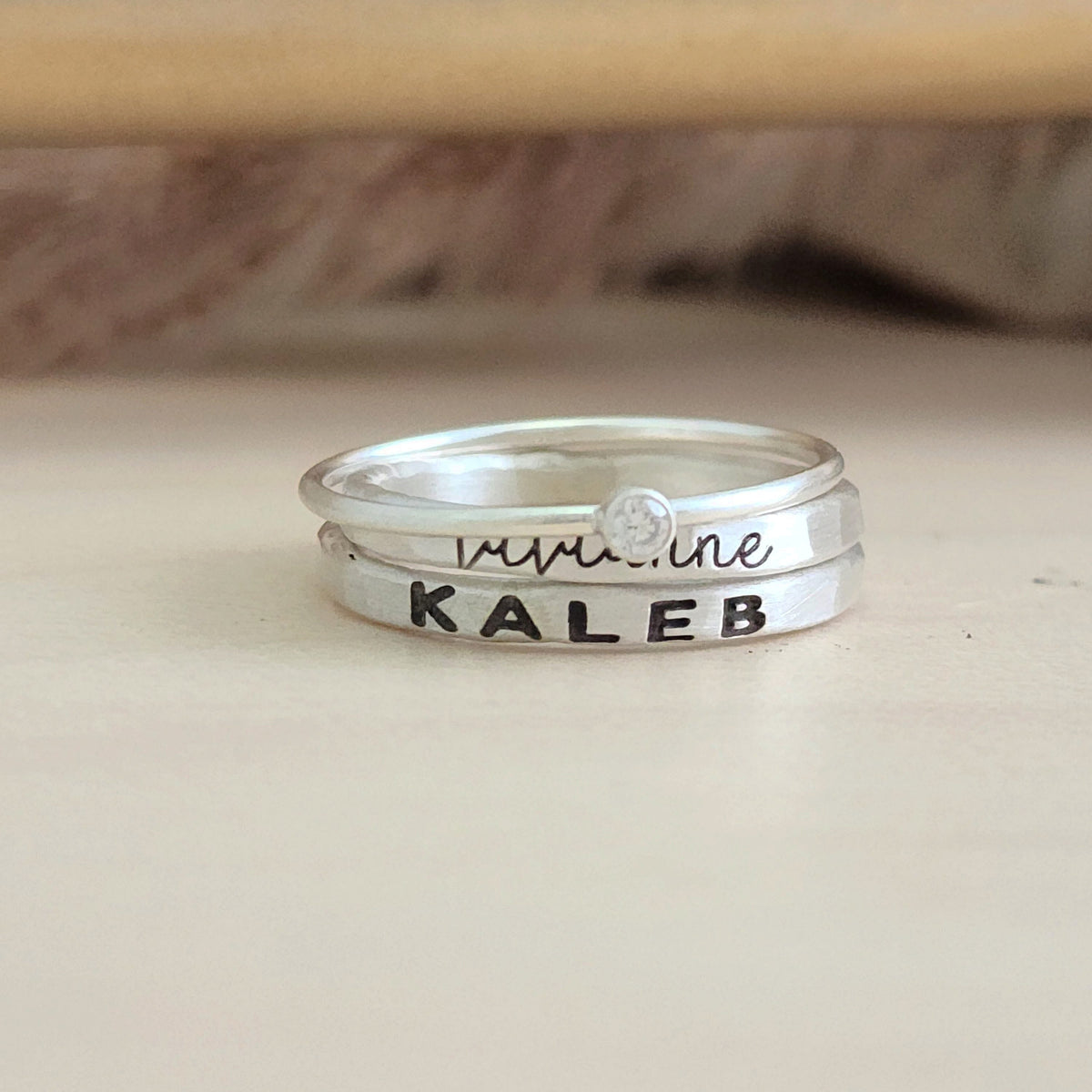 A set of sterling silver rings, including one with a clear cubic zirconia, and two with engraved names in different fonts.