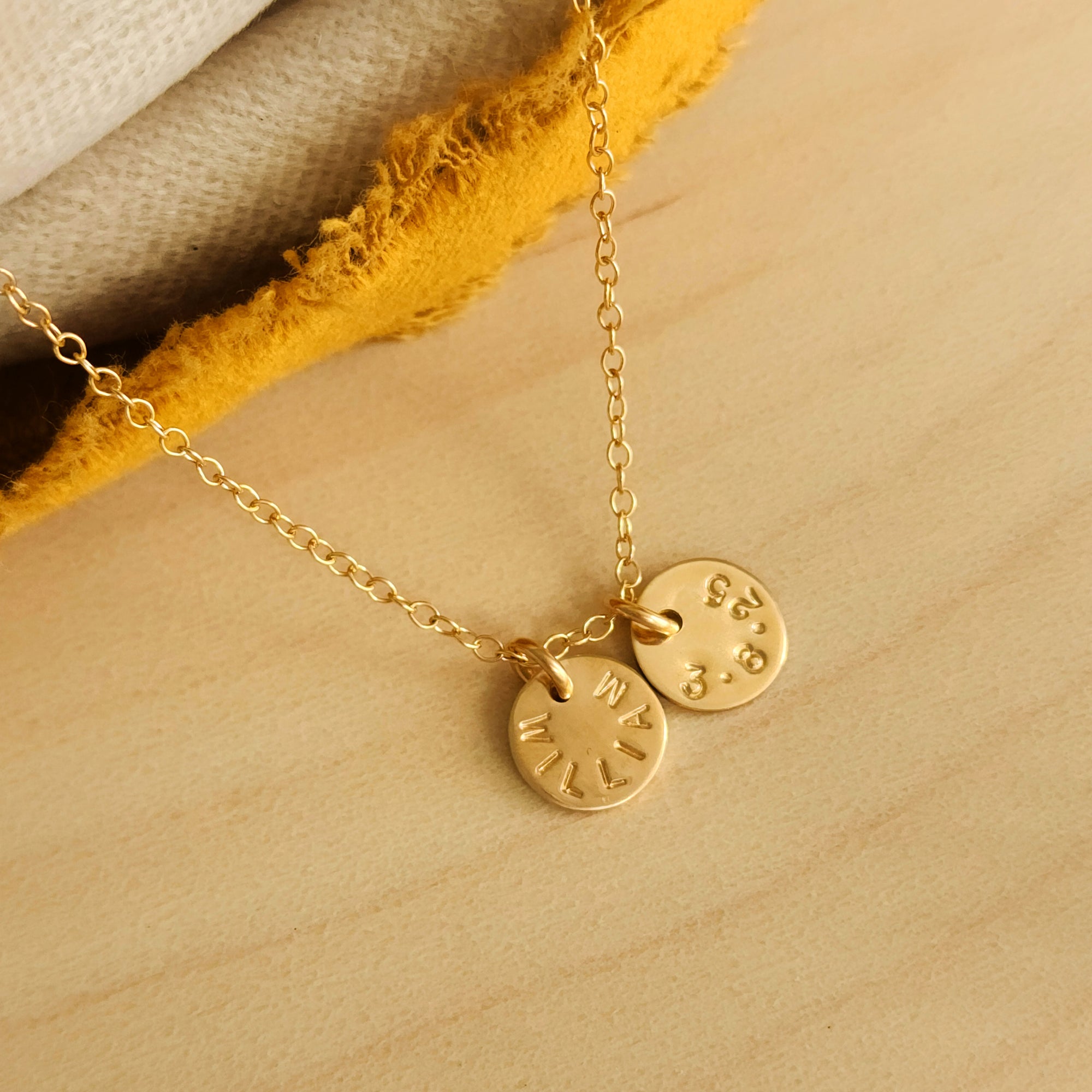 Close-up of 14K solid gold name necklace with two personalized round charms on wood background