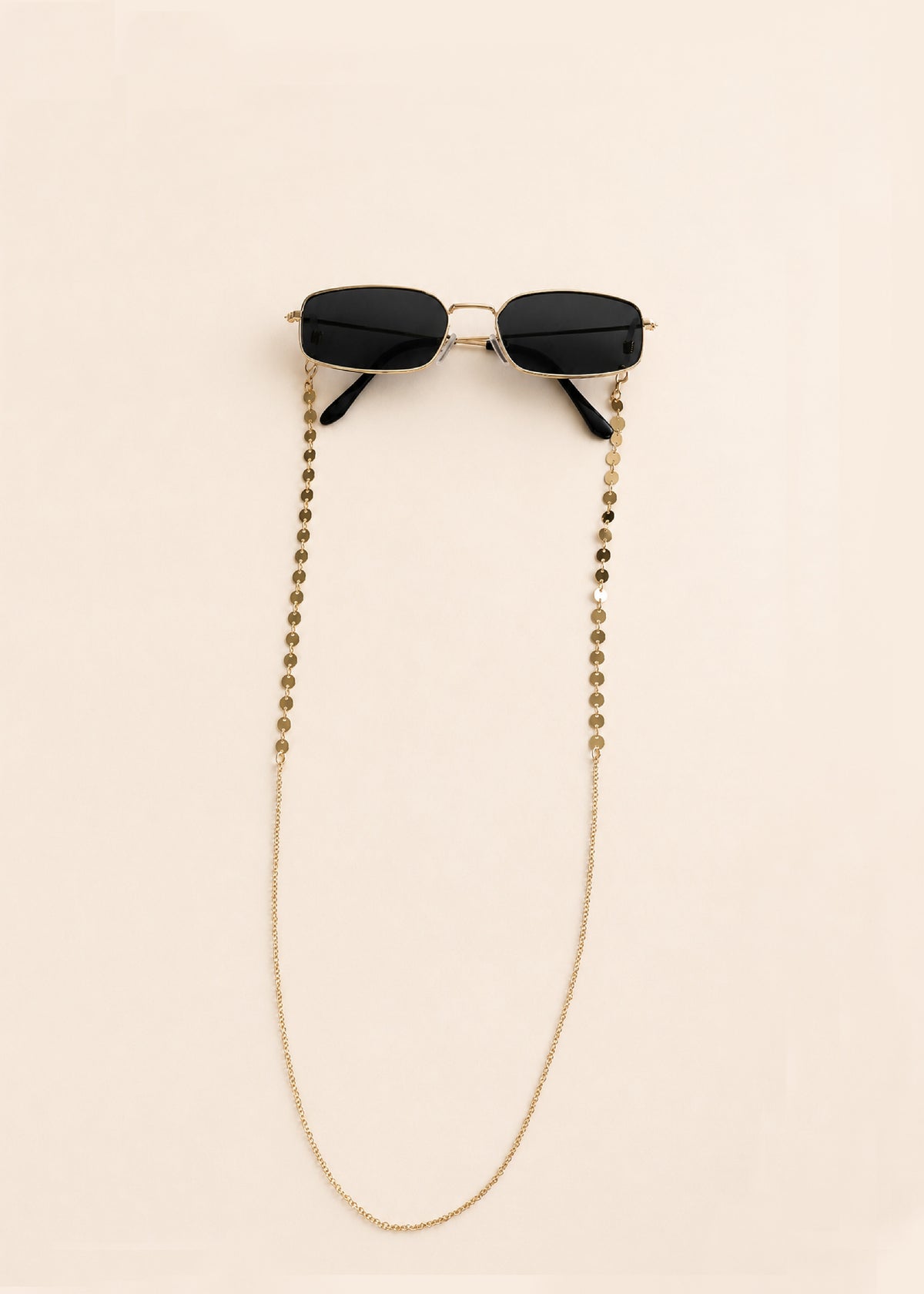 Black sunglasses with a gold chain on a beige background