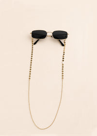 Black sunglasses with a gold chain on a beige background