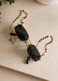 Black sunglasses with a gold chain on a light surface