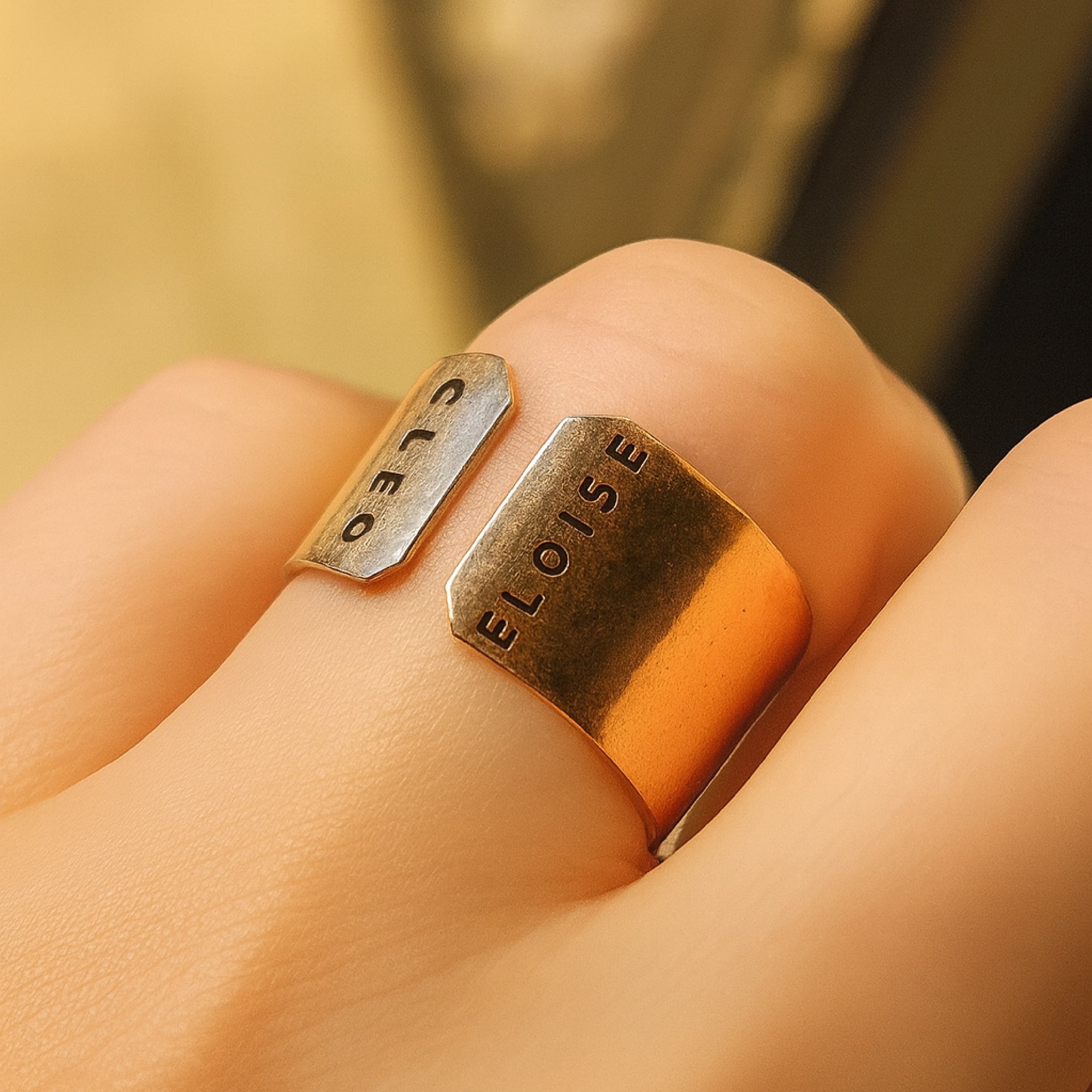 One gold ring with &#39;ELOISE&#39; and &#39;CLEO&#39; engraved on a finger against a blurred background