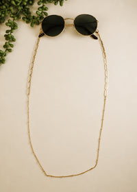 Sunglasses with a gold chain on a beige background