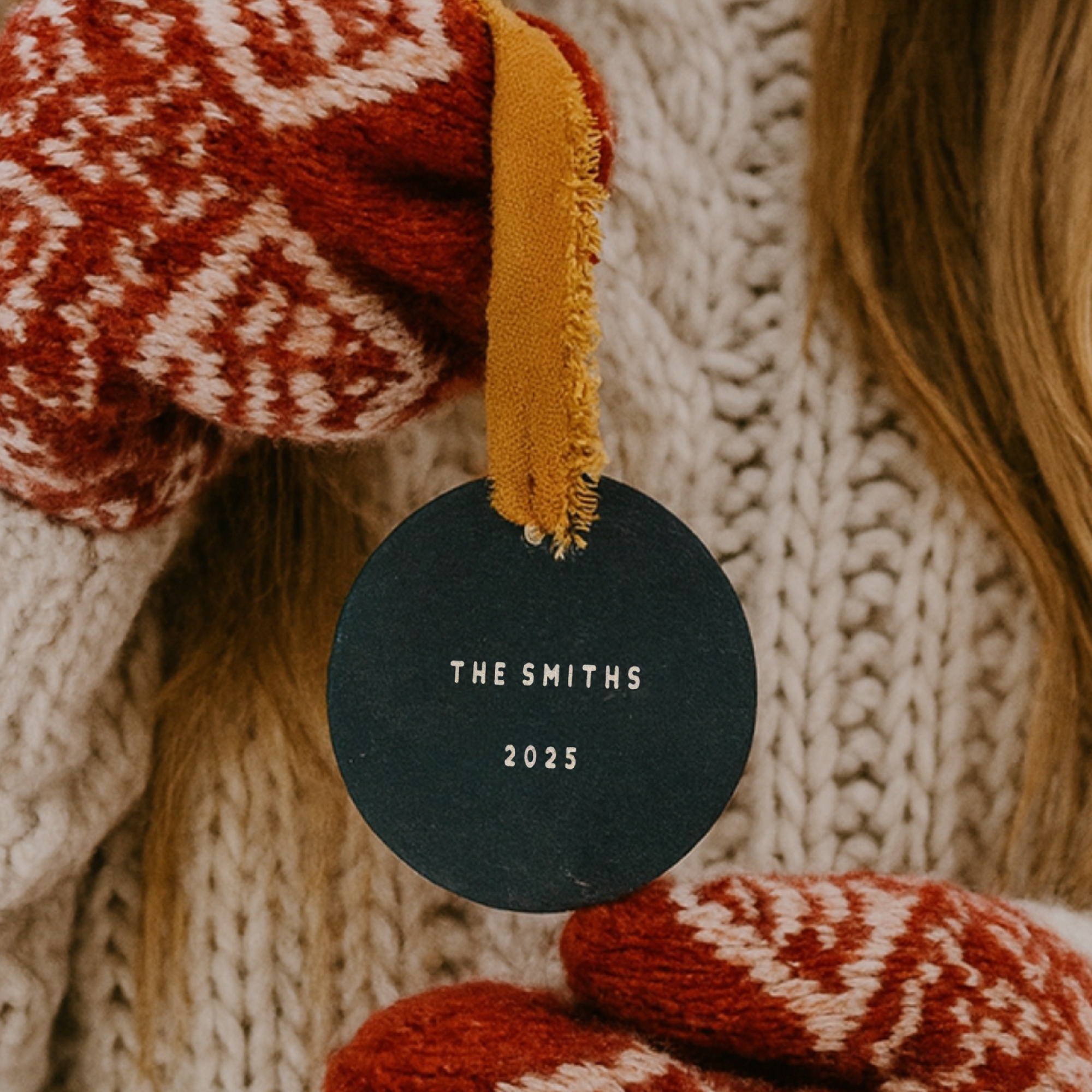 Black round ornament with 'THE SMITHS 2025' text, surrounded by red and white patterned fabric and yellow tassel.