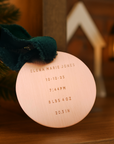 Wooden ornament with engraved birth details on a wooden surface with a blurred Christmas tree and lights in the background.