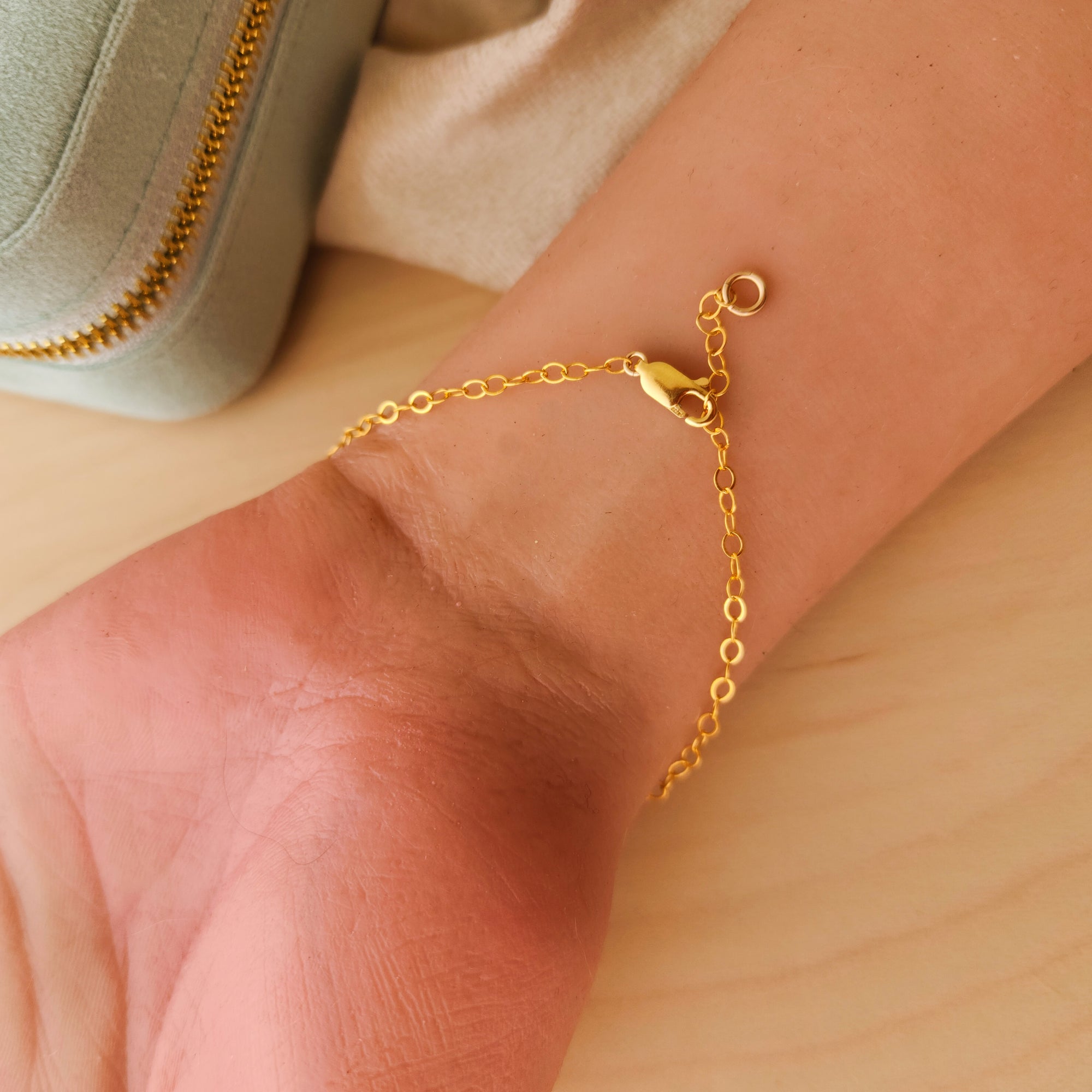 Gold bracelet lobster clasp close up on a wrist with a neutral background