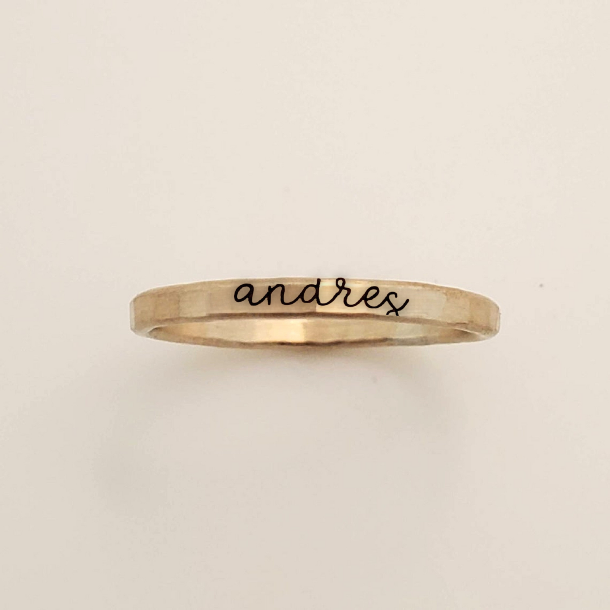 Gold ring with 'andres' engraving on a beige background