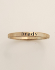 Gold ring with 'brady' engraved on a beige background
