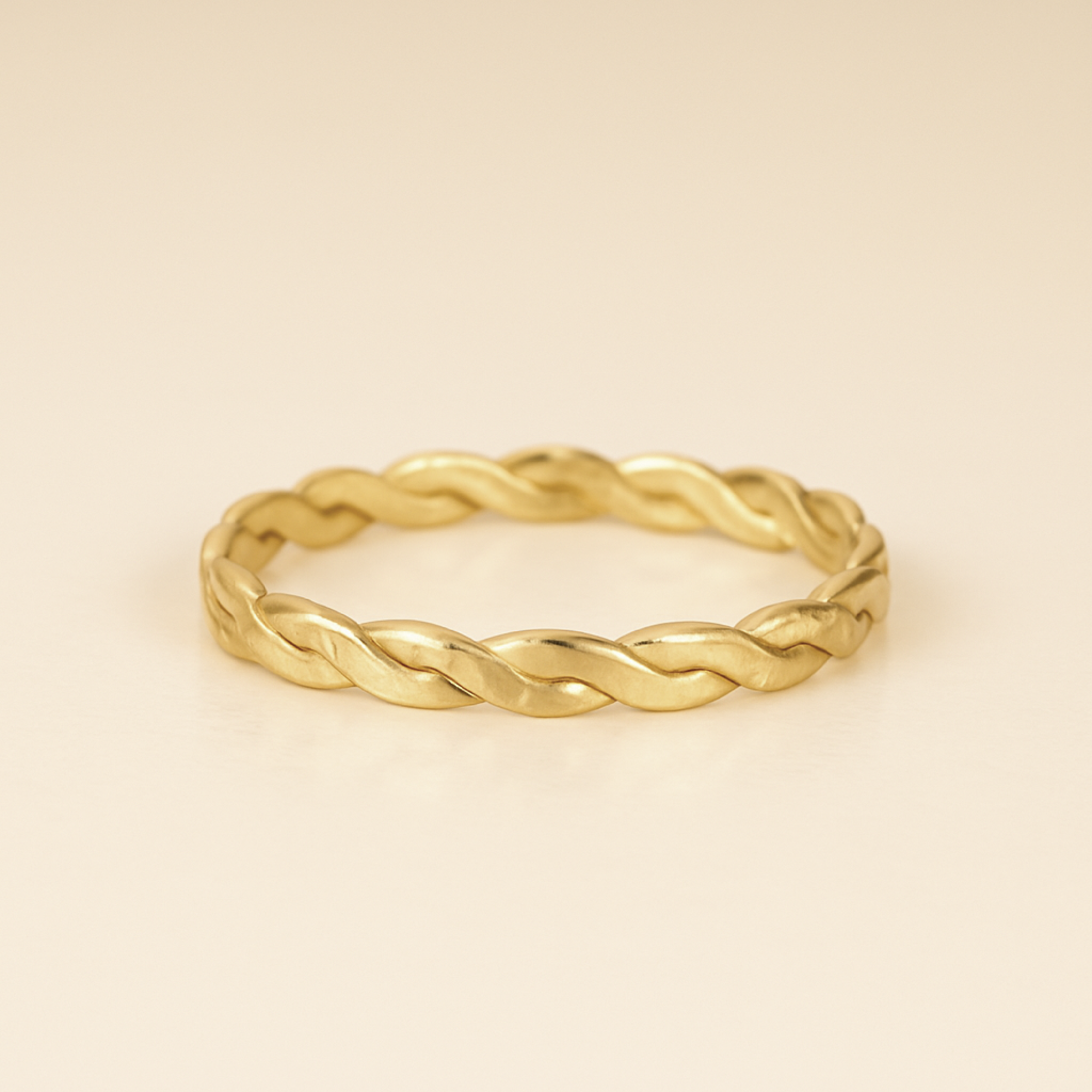 Gold braided ring on a beige background