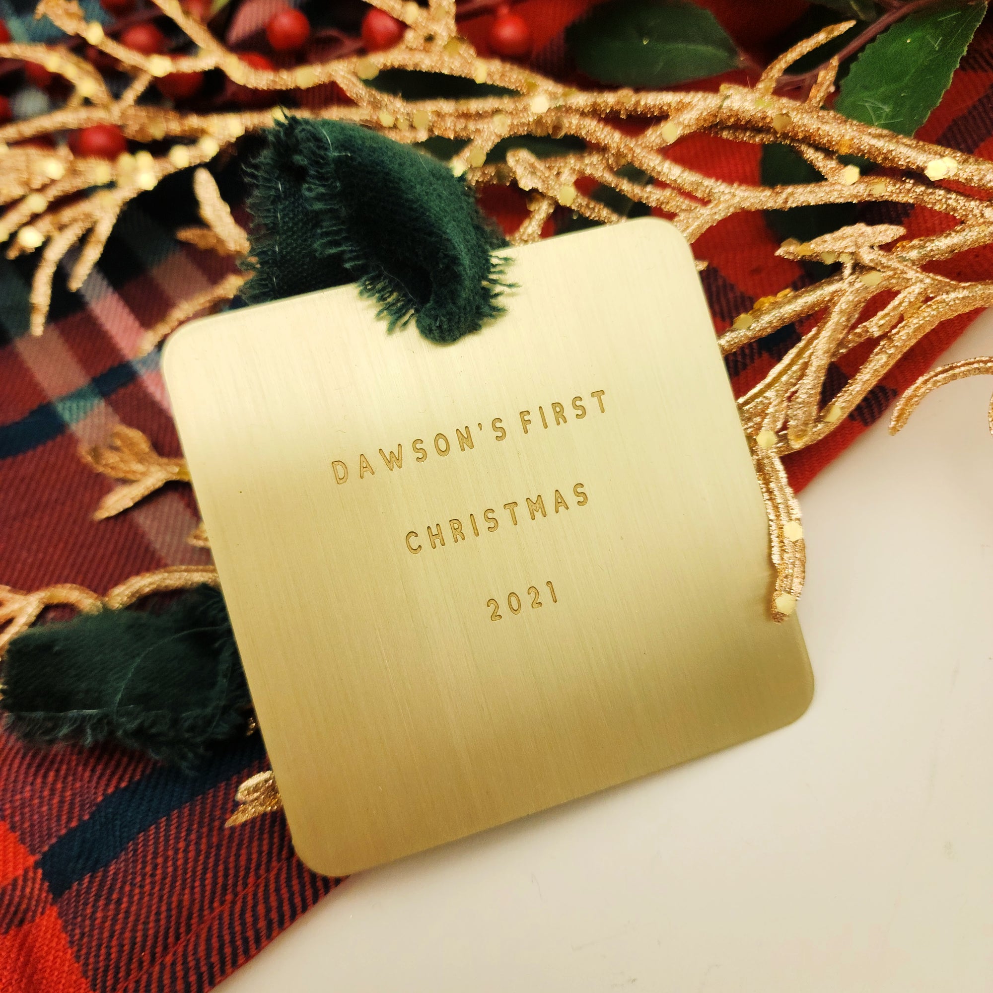 Gold ornament with 'Dawson's First Christmas 2021' text on a plaid fabric background.