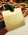 Gold ornament with 'Dawson's First Christmas 2021' text on a plaid fabric background.