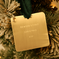 Gold ornament with 'Dawson's First Christmas 2021' text on a Christmas tree.