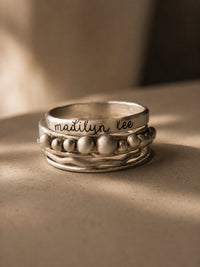 Silver ring with engraved name on a beige surface