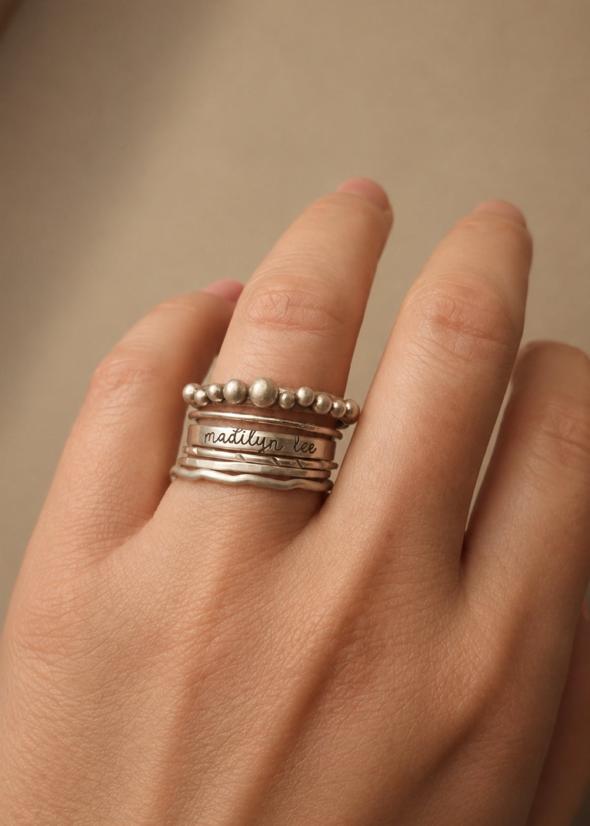 Hand wearing multiple silver rings with engraved text on a beige background