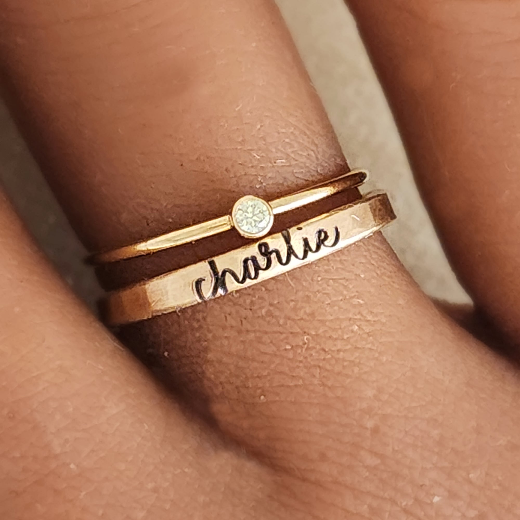 A photo showing a gold-colored ring with the name 'Charlie' engraved on it, worn on a person's finger.